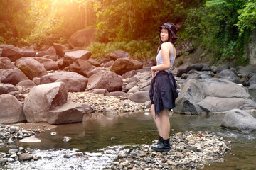 Young Asian Woman Standing on Rocky Riverbank in Forest During Outdoor Adventure