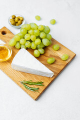 Delicious cheese platter with grapes, olives, and olive oil on wooden board