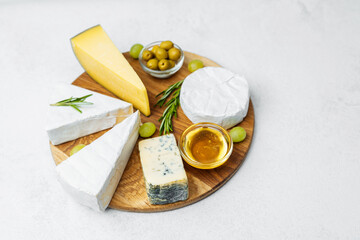 Cheese platter with honey, olives, and grapes on a wooden board