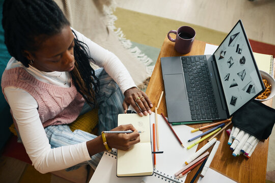 Woman writing in a notebook while surrounded by a variety of study materials and an open laptop on a wooden table, showing a productive workspace - Powered by Adobe
