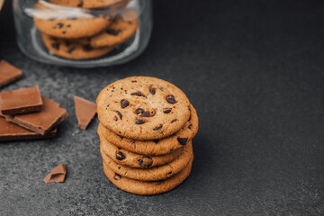 Cookies stacked next to chocolate pieces on a dark surface during a cozy moment