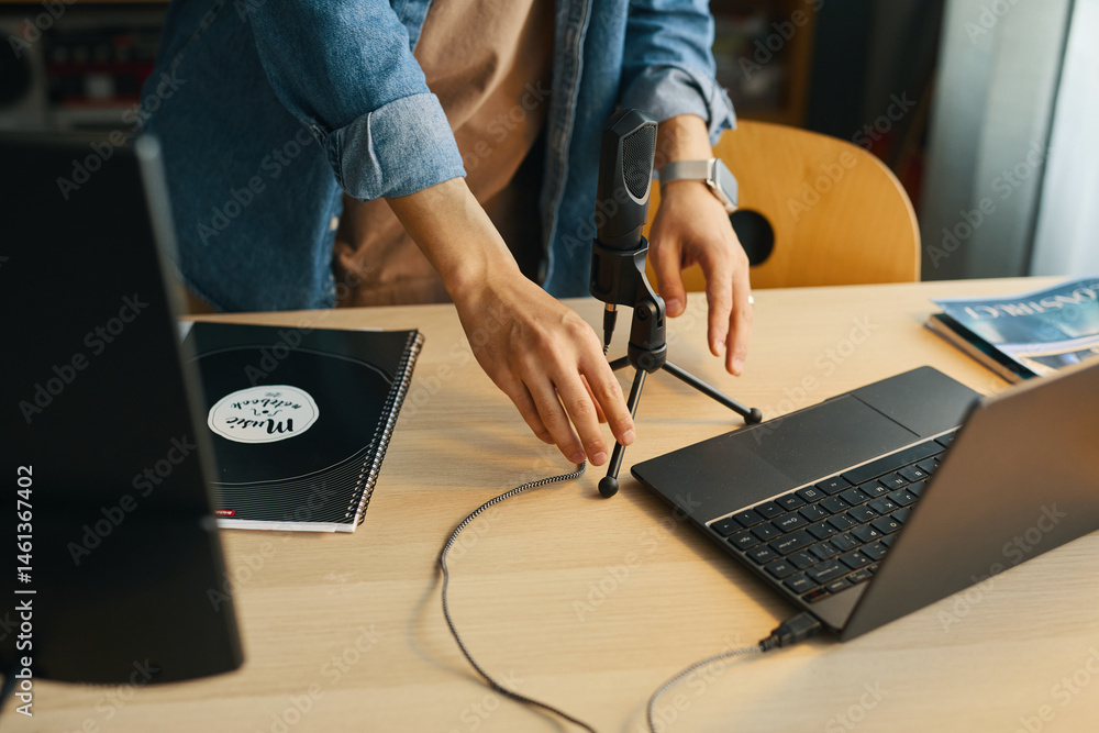 Poster close-up shot of male hands adjusting microphone on desk while using laptop and notebook report on d