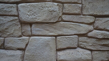 A close-up of a beige-toned stone wall constructed with irregularly shaped stones fitted together,...