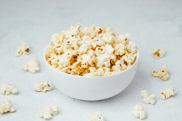 Fluffy popcorn in a white bowl surrounded by scattered kernels