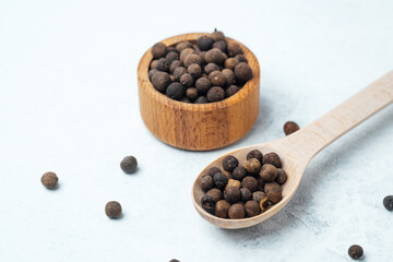 Whole allspice berries in a wooden bowl and spoon on light background