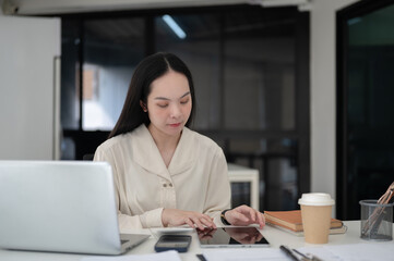 Fototapeta premium Female office worker or businesswoman looking at tablet while sitting at working table in office.