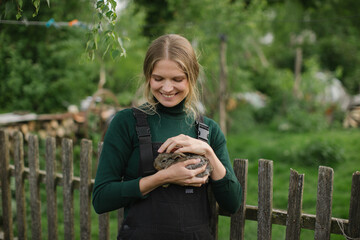 Young beautiful woman farmer with a baby rabbit in her hands on the background of the countryside.
