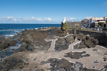View of old fishing village Garachico with sea pools and lava rocks village center in Tenerife canary island spain with blue sky white clouds background