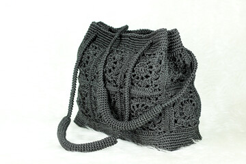 Black bag knitted with square motif and rectangular base isolated on white furry blanket.