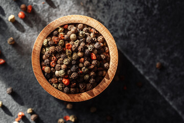 Colorful peppercorns in a wooden bowl on a dark surface with natural light