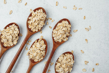 Oats arranged in wooden spoons on a light textured surface