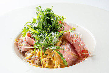 A plate of pasta garnished with fresh arugula, thinly sliced ham, and grated cheese. The dish is elegantly presented in a white bowl, highlighting its appetizing colors and textures.
