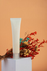 Cosmetic product in tube, bottle, lotion or serum and dried flowers with stylish props on cream background. 
