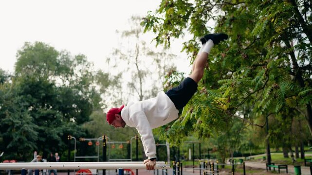 A young man performs impressive calisthenics exercises on parallel bars in a park, showcasing strength, balance, and fitness. He executes handstands and other dynamic moves,