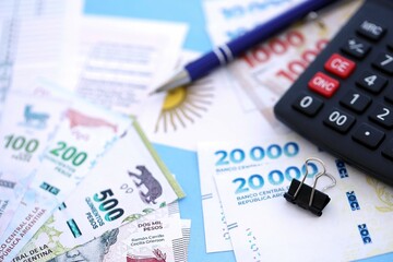 Argentine pesos money bills in big amount lies on table with pen, calculator, passport and tax forms