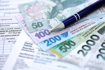 Argentine pesos money bills in big amount lies on table with pen and tax forms close up