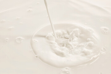 Milk stream hits white liquid creating splash and swirl in soft lighting. Concept of drink, organic food, aesthetics, advertisement