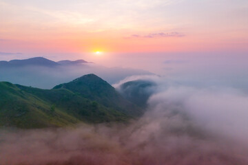 Morning light from the sun dawn on the coast with mountains and hills shrouded in wet clouds and fog, warm tones summer aerial above point view landscape