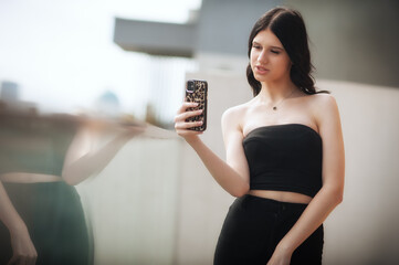 A fashionable young girl poses for a selfie against a stylish urban backdrop, showcasing her modern outfit