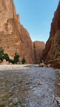 A river flowing through the deep Todra gorge in morocco. Towering reddish-brown rock cliffs under a clear blue sky.