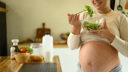 Happy pregnant woman eating a fresh salad, promoting healthy eating habits during pregnancy