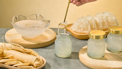 A hand holding a golden spoon is scooping bird's nests. Around it are unprocessed bird's nests and...
