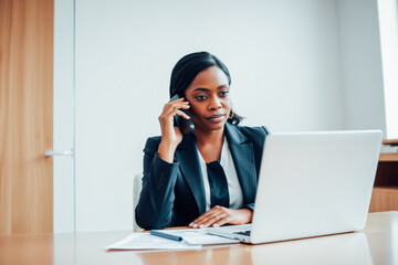 Focused Businesswoman Multitasking on Phone and Laptop