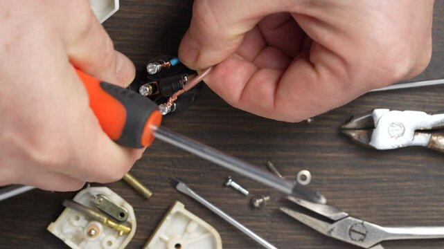 Using a Phillips screwdriver, loosen the screw on the white electrical power plug, close up. The process of parsing the body of plastic electrical plug. Repair and maintenance of electrical equipment