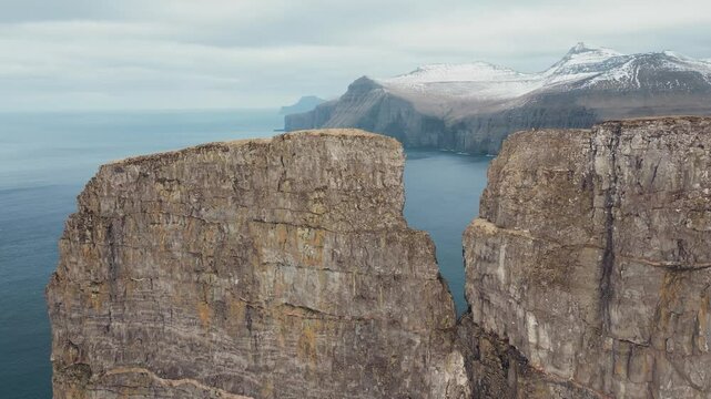 Drone scenery of Eidiskollur cliff with views of the surrounding ocean and snowy rugged terrain