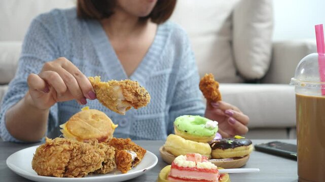 Unhealthy woman with binge eating disorder enjoying fast food like fried chicken, burgers, donuts, and sugary desserts, showing signs of sugar addiction, salty snack cravings, and high-calorie, fat