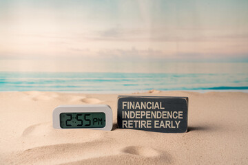 Digital clock and sign reading "Financial Independence Retire Early" on sandy beach, showcasing concept of early retirement and financial freedom