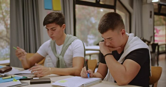 Two focused students work together on an assignment in a classroom setting after class. They review notes and collaborate to complete their tasks in a studious learning environment.