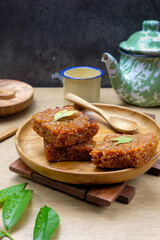 Traditional Asian sticky rice cake, known as Wajik, made from glutinous rice and palm sugar served on a wooden plate with tropical leaves and a cup of tea in the background.Suitable for Asian cuisine.