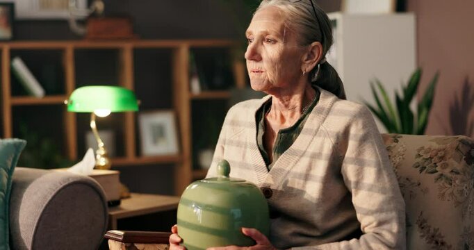 Thinking, urn and sad with old woman on sofa for reflection, mourning and retirement. Memory, mental health and grief mindset with senior person in living room at home for depression, loss and death