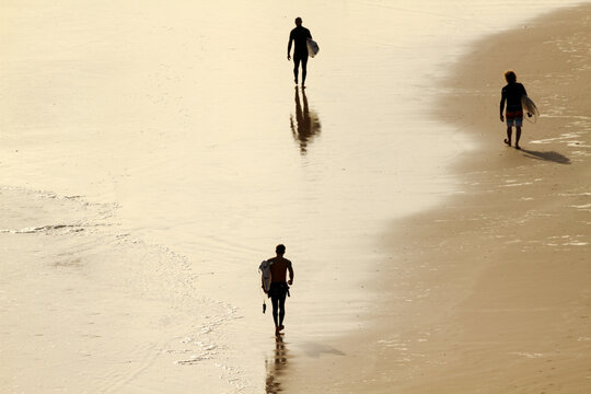 Three men walking along beach with surfboard under their arms.