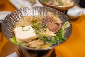 Japanese hot pot dish with beef, tofu, enoki mushrooms and greens simmering in a light broth served in a metal bowl over flame