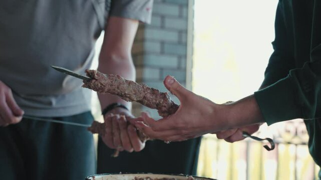 Skilled chefs forming minced meat onto skewers, creating traditional lula kebab with precise technique in professional kitchen environment