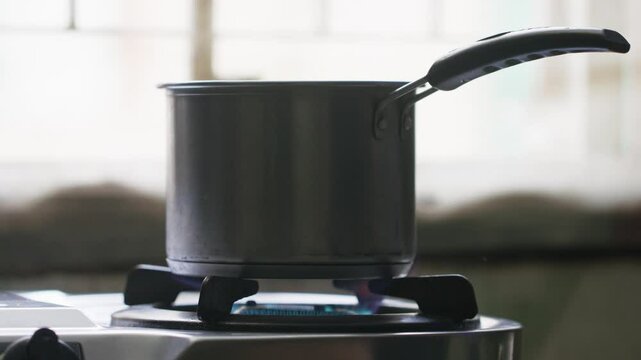 A metal cooking pot on a stovetop and a hand lit the stove with a matchstick