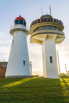 An old lighthouse next to a new light tower with sunlight shining between them
