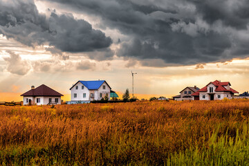 Small buildings in the field under stormy clouds at sunset