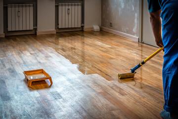 Worker varnishing floor with Eco white acrylic varnish for wood parquet floor, lacquering roller. Home renovation. Industrial tools