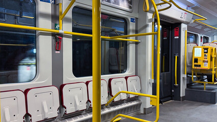 Empty urban train interior with yellow poles and red straps on a calm day, featuring colorful designs and modern public transportation elements
