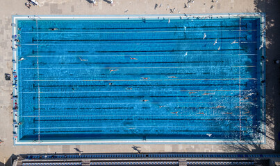 Top-down aerial view of swimmers training in an outdoor swimming pool with clear blue water and...