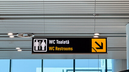 Airport restroom signage with male and female symbols and directional arrow under modern ceiling at...