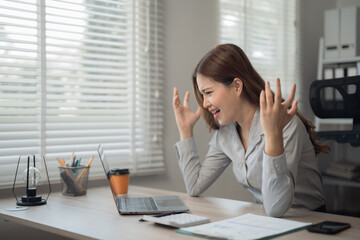 Obraz premium Young frustrated businesswoman working at office desk in front of laptop, she is stressed and disappointed with her work, having problems and feeling desperate