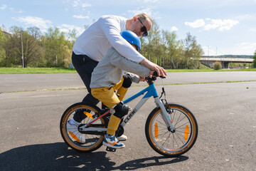 Naklejka premium Bad Hersfeld, Germany, 04.21.25. Parent Teaching Child to Ride Bicycle in Park