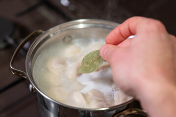 Adding bay leaf to enhance flavor in boiling dumplings for a comforting meal. A hand adds a bay...