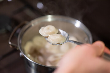 Boiling dumplings in a metal pot on a stovetop for a hearty meal. Dumplings boil in a stainless steel pot as man checking readiness with a spoon