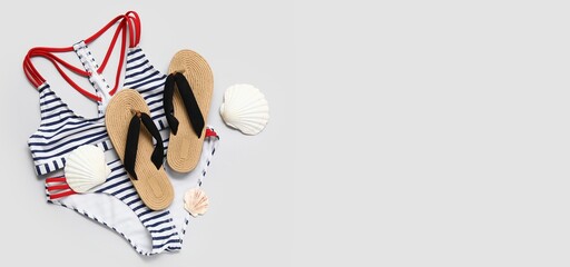 Stylish swimsuit, flip-flops and sea shells on light background with space for text