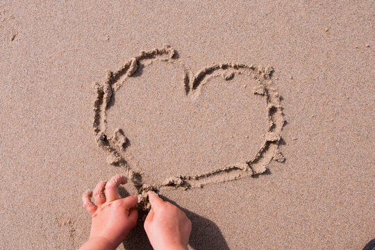 Child hands drawing heart shape on beach sand